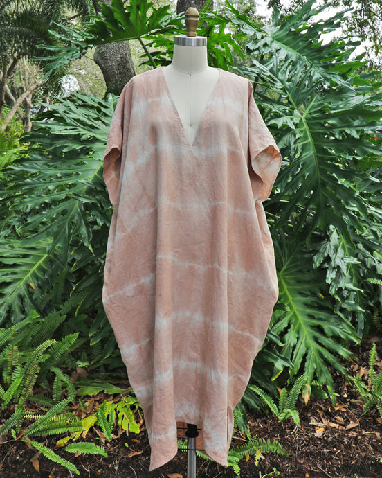 pink tie dye caftan draped on body form in front of tropical plant background