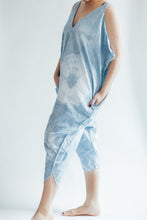 Load image into Gallery viewer, 3/4 view of model wearing indigo dyed jumpsuit with left leg forward and hands in pockets.
