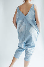 Load image into Gallery viewer, back view of model wearing the indigo dyed jumpsuit. leaning on right leg with hands in pockets. Low v-neckline at back.
